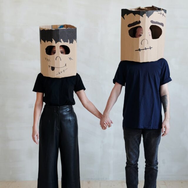 a couple wearing diy cardboard box mask while holding each other s hands